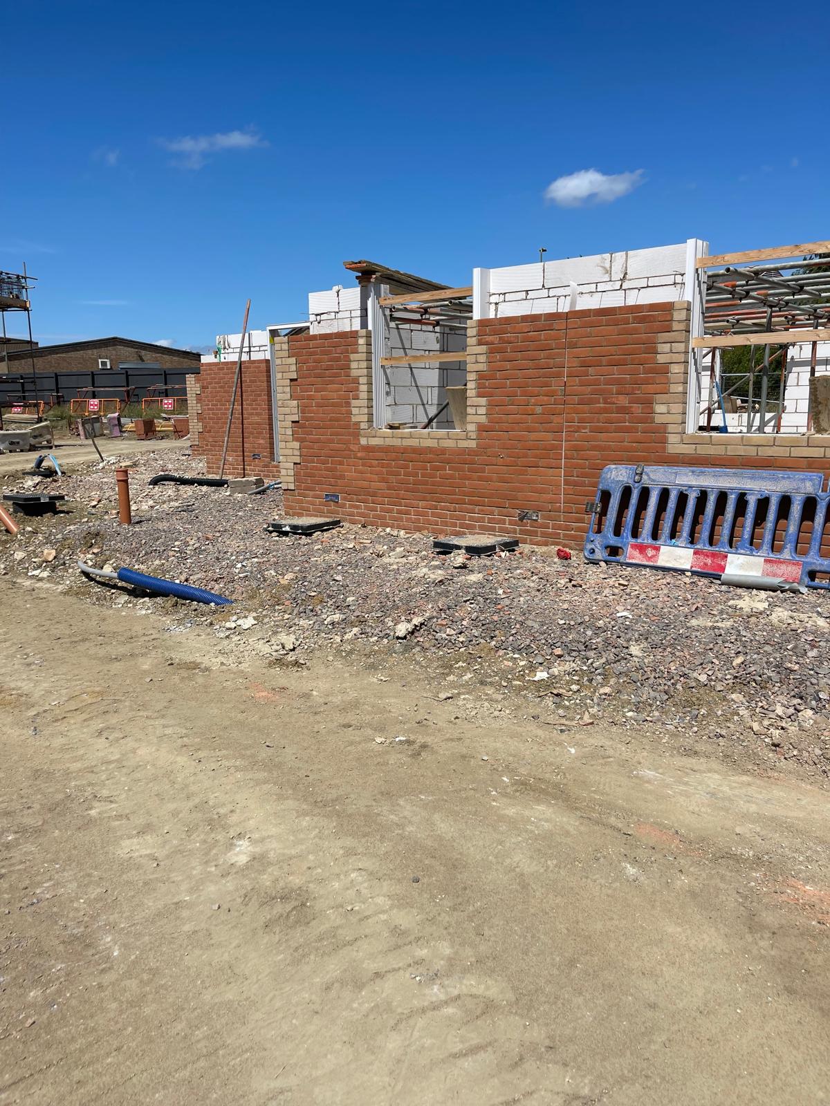 New-build house walls in red brick with toothed buff brick reveals around window openings, white aerated blockwork rising behind and scaffolding beyond