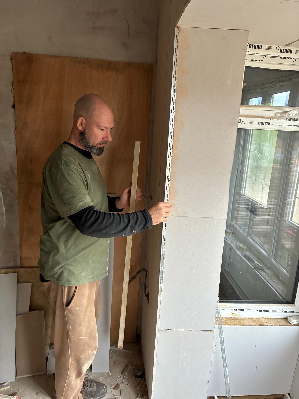Builder fixing metal angle bead to a plasterboarded archway reveal beside a new uPVC window