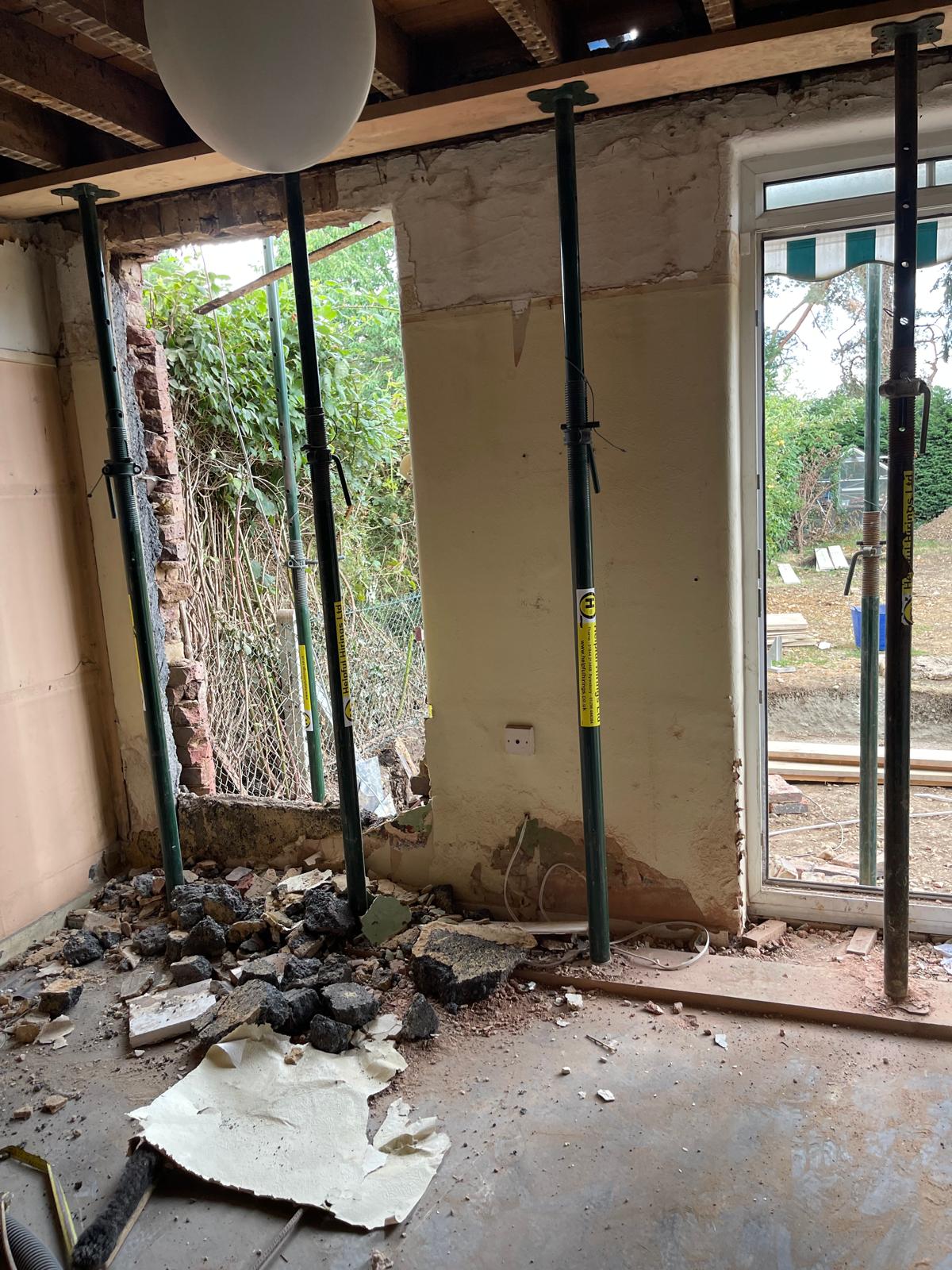 Interior with acrow props under the ceiling joists, a section of external wall knocked through to the garden and rubble on the floor