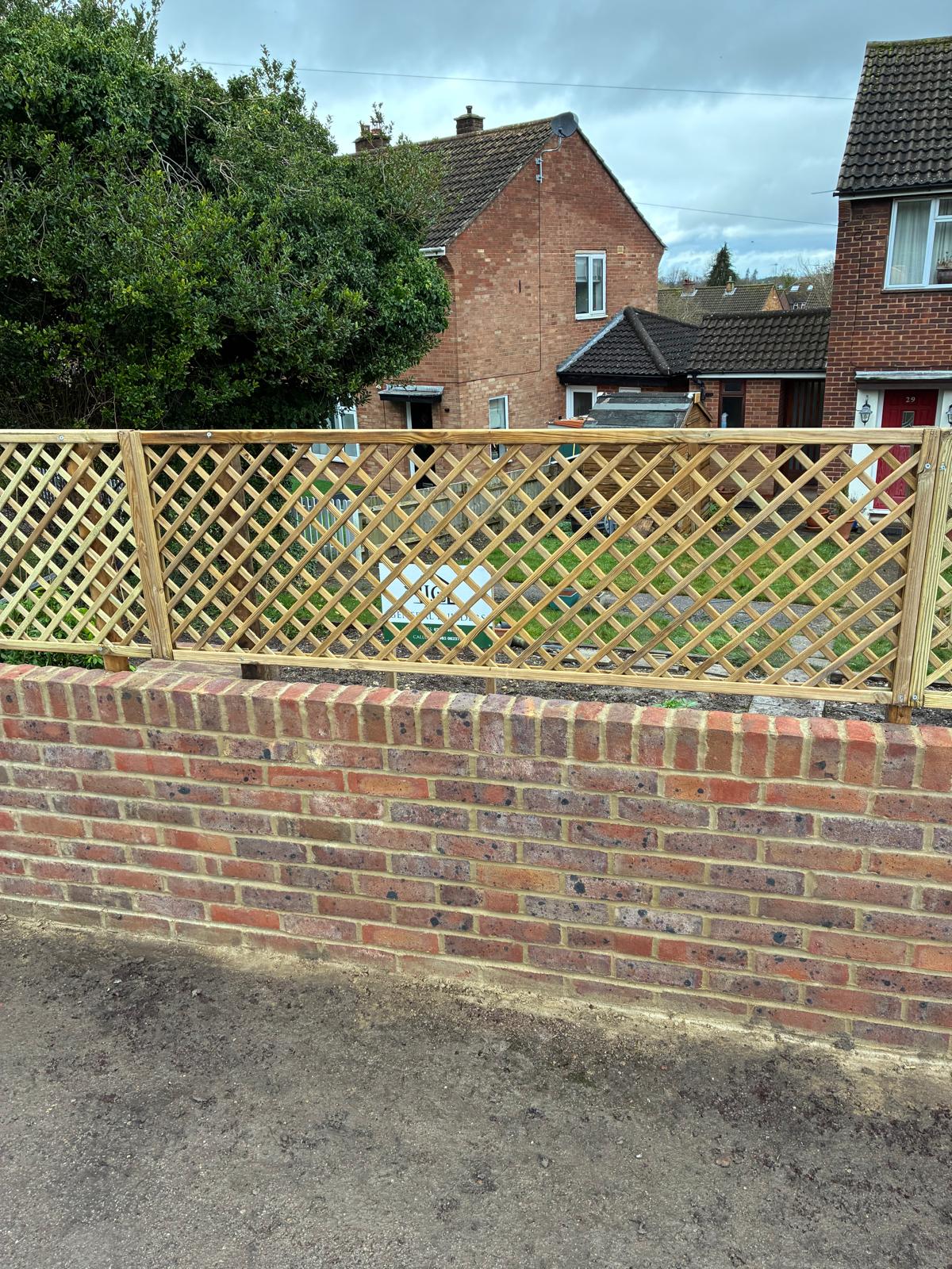 Newly built red brick front garden wall topped with timber diamond trellis panels, with a J.C General Builders sign in the garden behind